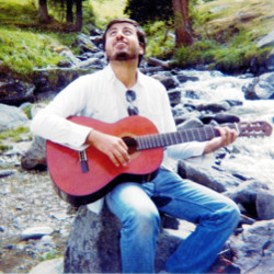 Claudio ventenne che suona la chitarra sulla riva di un fiume di montagna